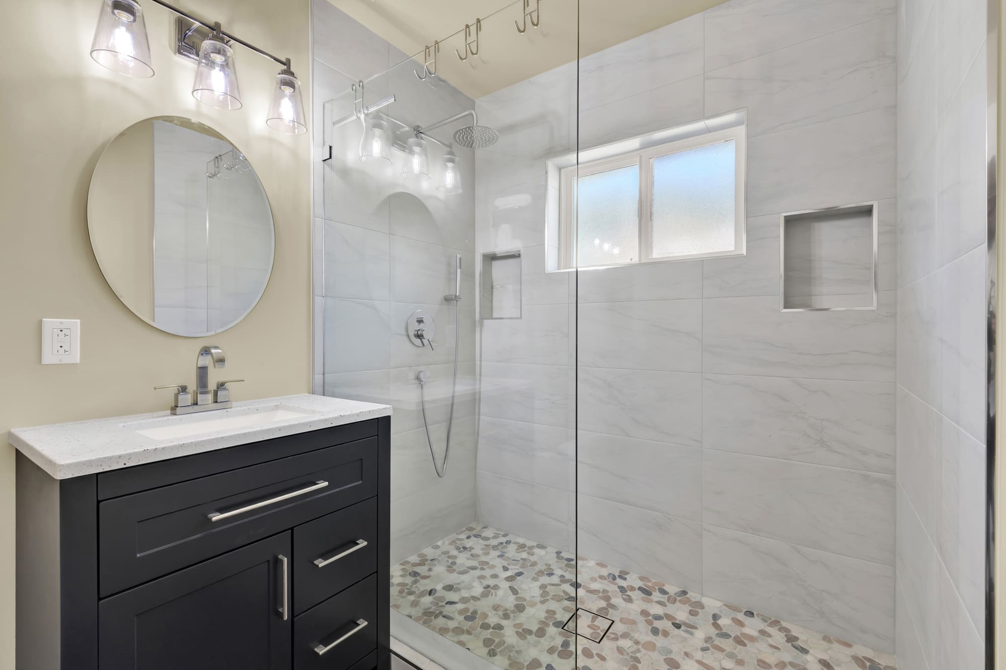 Marble-look porcelain runs floor to ceiling with a recessed niche and a river-rock pebble floor. Tile this size only lines up if the layout is set before the first cut.