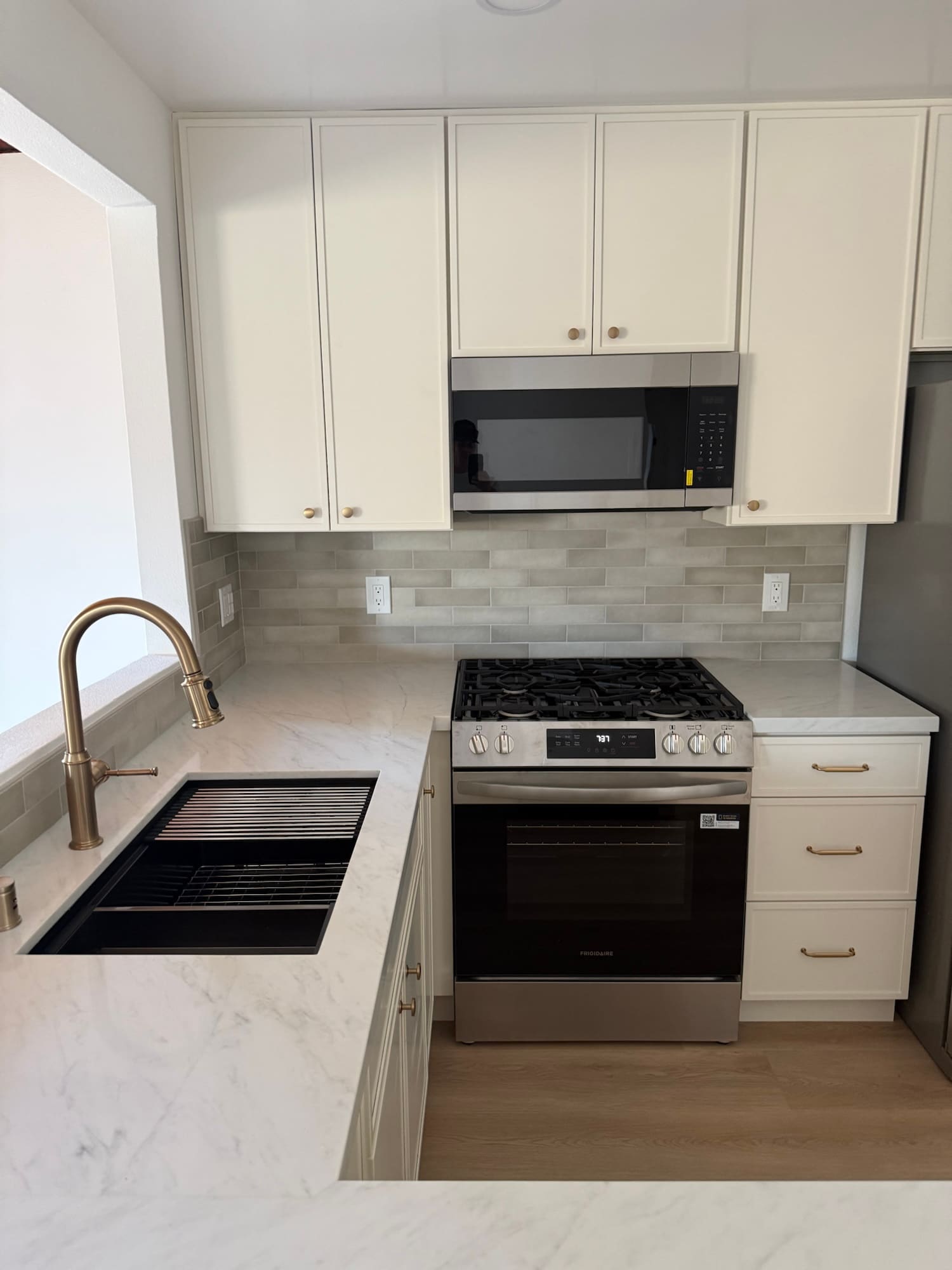 Shaker cabinets to the ceiling, quartz counters, and a stacked tile backsplash. Champagne bronze faucet and pulls over a black composite sink.