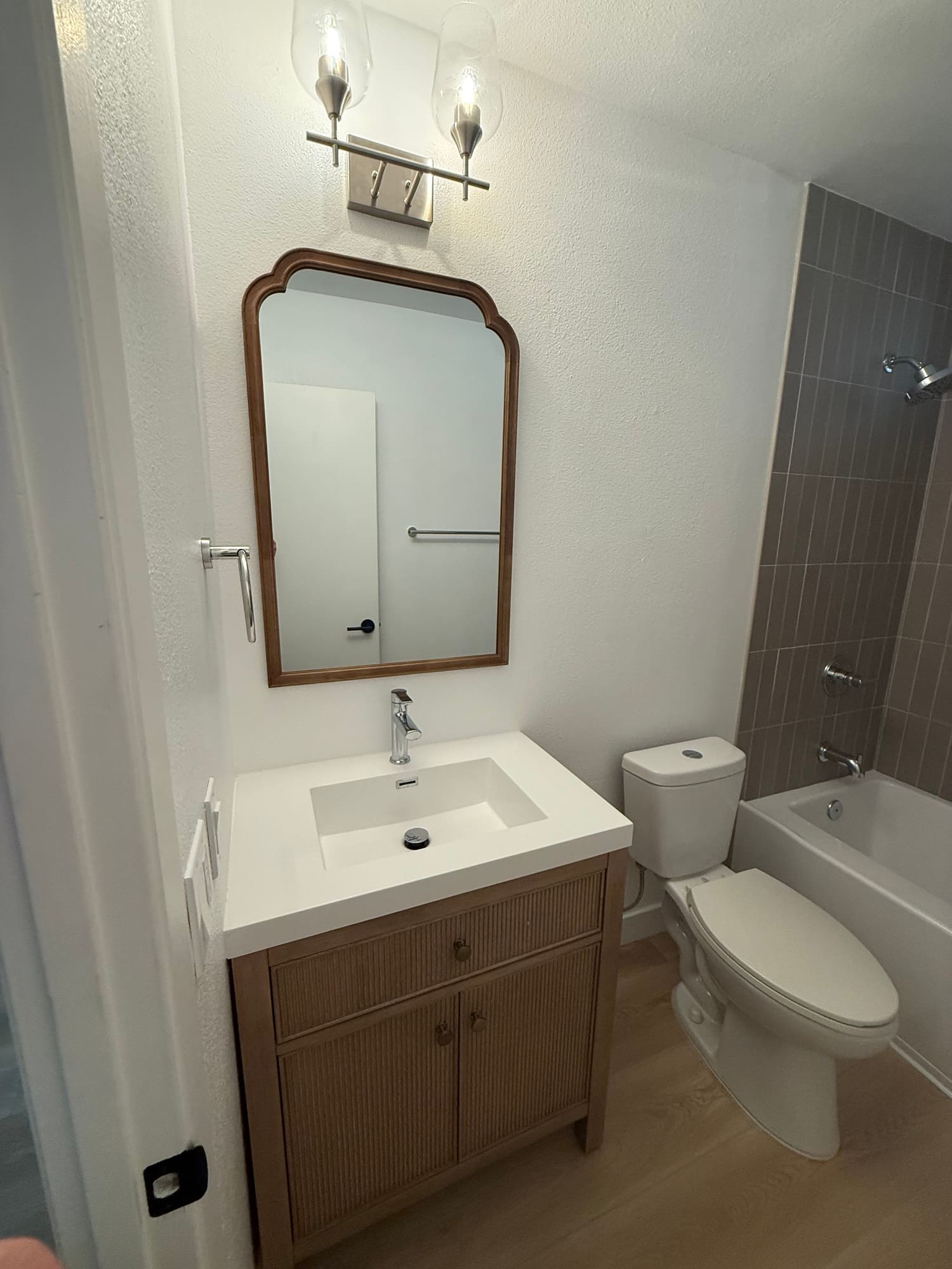 The hall bath: a reeded wood vanity with an integrated top, an arched mirror, and chrome fixtures.