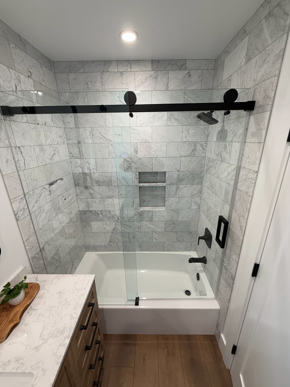 A soaking tub set into a marble surround, with a glass shower on a black rail alongside it. The stone was laid out so the veining runs continuous.