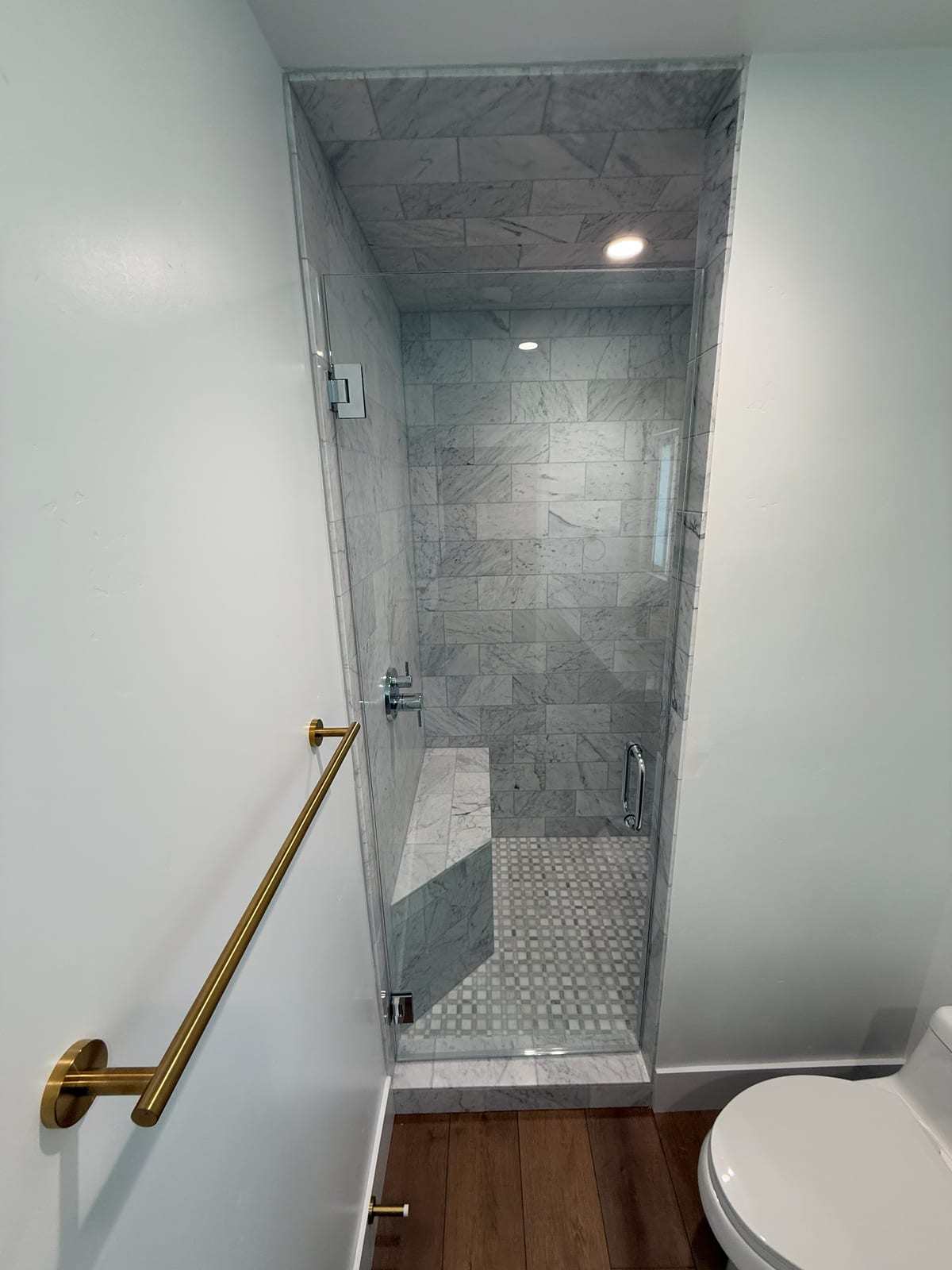 Another full bath: a frameless glass walk-in shower with gold fixtures, a built-in bench, and marble tile run floor to ceiling over a pebble floor.